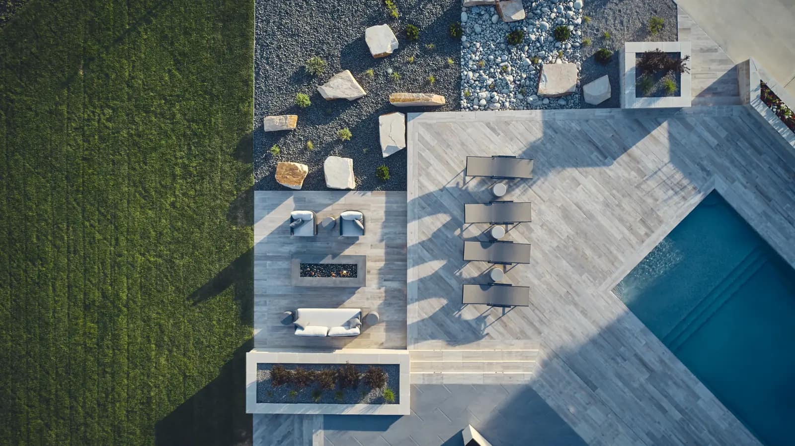 Aerial of the pool deck with chaise lounges, planters, fire lounge, and adjoining lawn