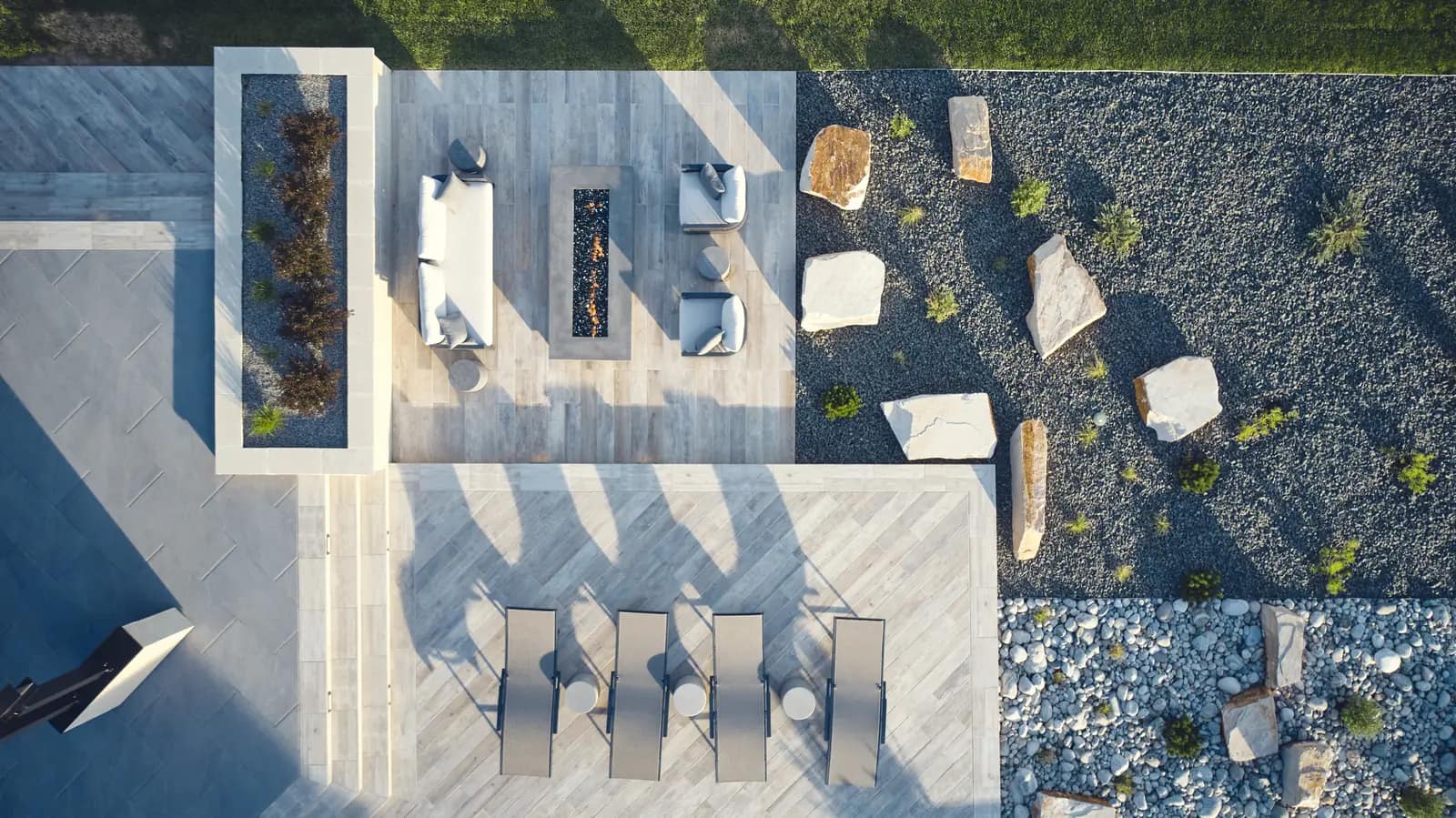 Aerial of a sunken lounge with outdoor sofas and a linear gas fire pit set in boulders and gravel