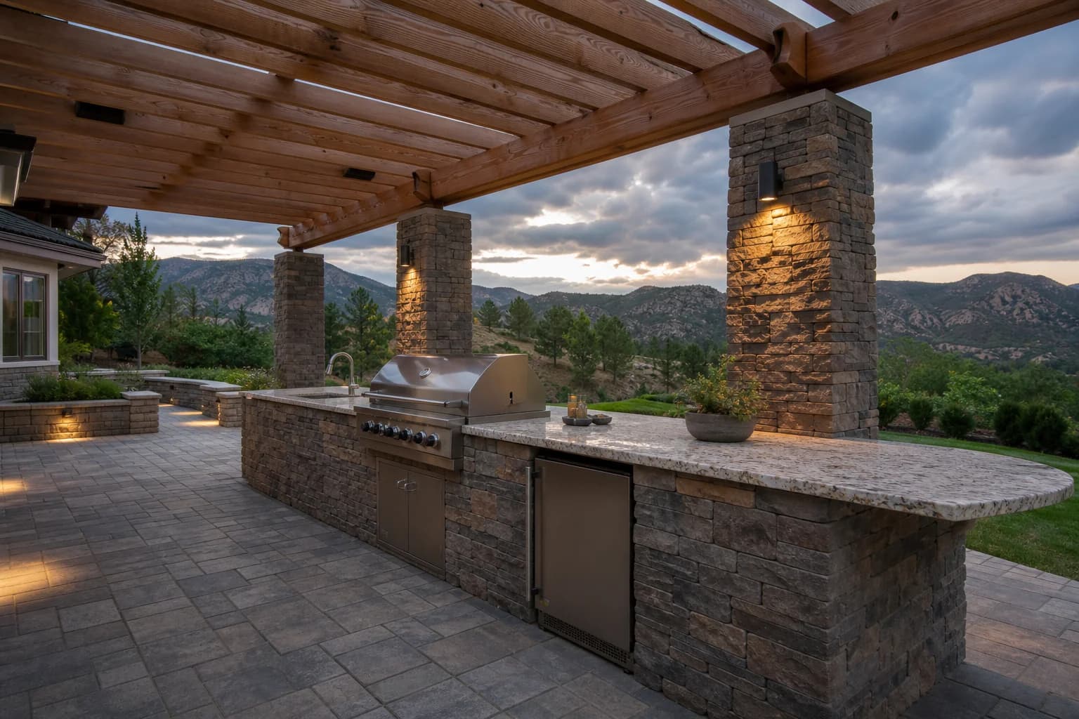 Granite outdoor kitchen island with stone fascia, cedar ceiling detail, and modular paver terrace